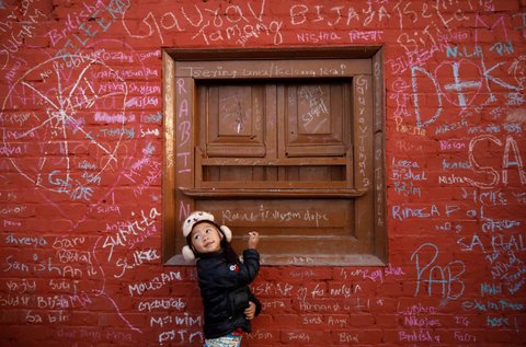 A girl looks towards her father as she writes on the wall of a temple

