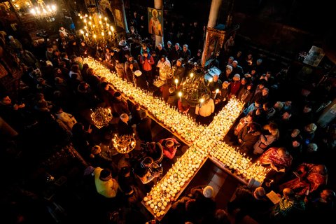 People pray around a cross-shaped platform covered with candles in jars of honey during a ceremony marking the day of Saint Haralampi, protector of beekeepers, at the Church of the Blessed Virgin

