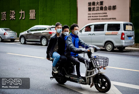 افرادی که ماسک صورت دارند با موتور سیکلت در شهر ووهان تردد می کنند
