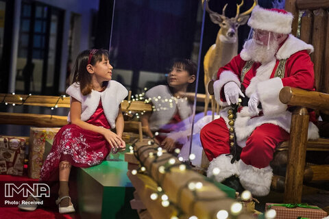 بابانوئل نقابدار از طریق یک مانع شفاف در یک فروشگاه Pro Bass با کودکان صحبت می کند
