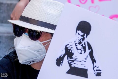 یک آسیایی با در دست داشتن تصویری از  بروس لی در تجمع علیه جنایات نفرت ضد آسیایی در مقابل تالار شهر لس آنجلس شرکت کرده است