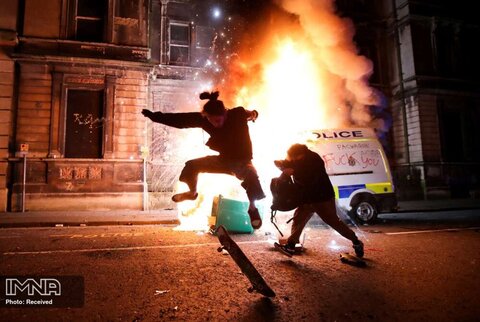 اسکیت کردن یک معترض به لایحه پیشنهادی جدید پلیس  بریستول انگلستان در مقابل ماشین در حال سوختن پلیس
