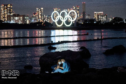 سلفی گرفتن یک زن و شوهر از پشت حلقه های المپیک روشن در ساحل اودایبا توکیو در ژاپن 