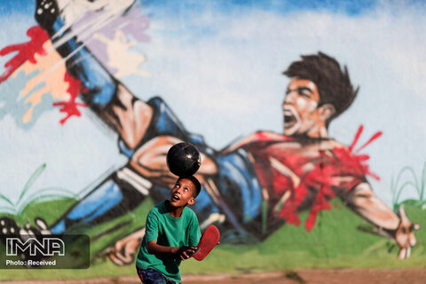 فوتبال بازی کردن کودکی در یکی از خیابان‌های محله سیلندیا در برازیلیا، برزیل