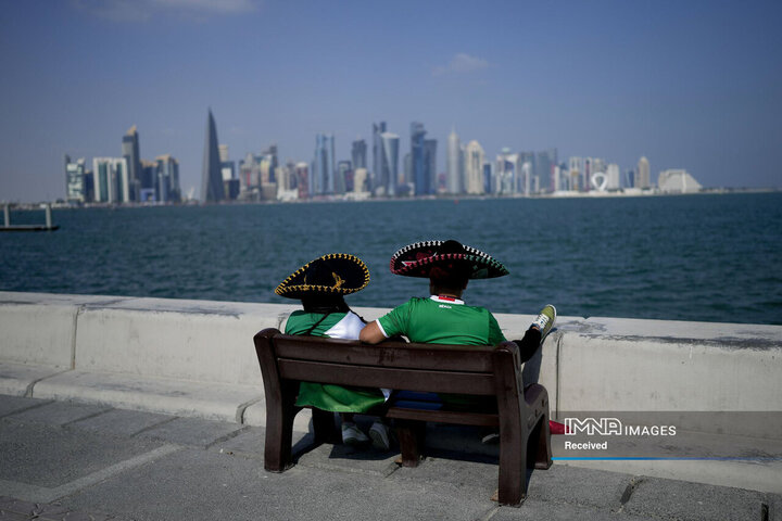 دو هوادار فوتبال مکزیک روی نیمکتی در دوحه قطر نشسته اند