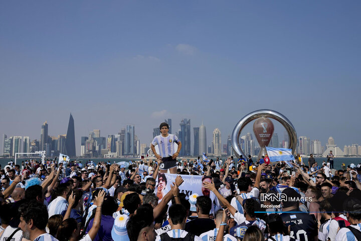 طرفداران فوتبال آرژانتین در دوحه، در حالی که تصویری از دیگو مارادونا فقید را در دست دارند، جمع شده‌اند.