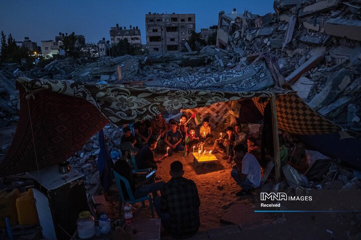 کودکان فلسطینی پس از تظاهرات کودکان این محله علیه حملات به غزه، در جریان آتش بس شکننده پس از درگیری ۱۱ روزه بین حماس و اسرائیل، با شمع در بیت لاهیا، غزه، فلسطین تجمع کردند.