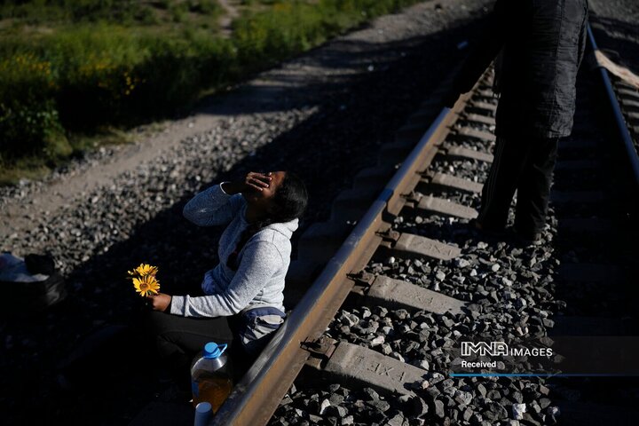 یک مهاجر ونزوئلایی هنگام شوخی با شوهرش که چند گلی را که در چمن چیده بود به او داد، می خندد، در حالی که آنها در امتداد خطوط راه آهن به امید سوار شدن به قطار باری به سمت شمال در Huehuetoca، مکزیک، در 20 سپتامبر 2023 منتظر هستند.
