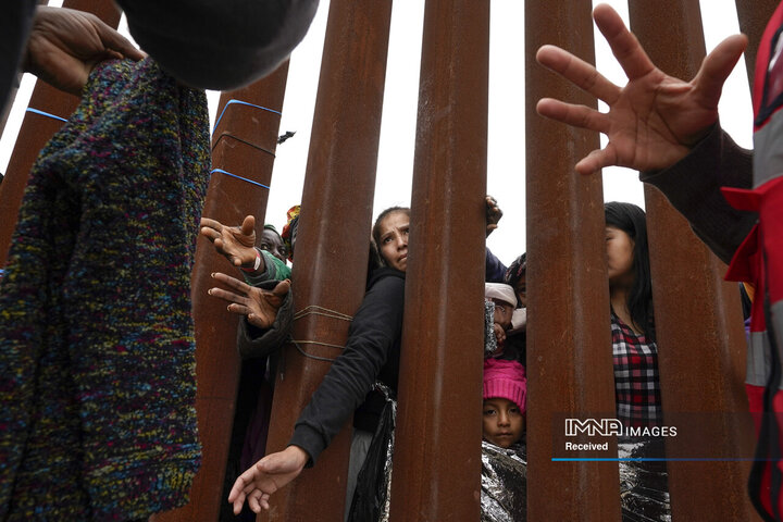 مهاجران در حالی که منتظر درخواست پناهندگی برای ورود به ایالات متحده در 12 مه 2023 هستند، لباس هایی را که داوطلبان در سن دیگو تحویل می دهند، از طریق دیوار مرزی می گذرانند.