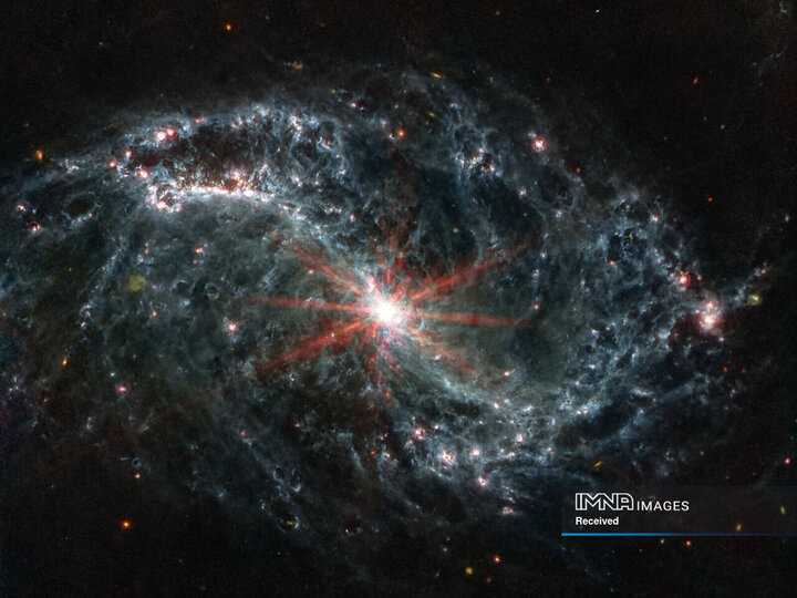 شبکه‌های پیچیده‌ای از گاز و غبار که در کهکشان مارپیچی تار مانند NGC 7496 در یک تصویر ترکیبی که توسط تلسکوپ جیمز وب گرفته شده و توسط ناسا در 16 فوریه 2023 منتشر شد، دیده می‌شود. هشت سنبله پراش قرمز از هسته بسیار درخشان آن خارج شده‌اند. نقاط رنگارنگ در پس زمینه نشان دهنده کهکشان های پس زمینه است.
