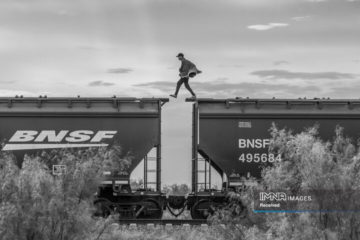 «یک مهاجر بر فراز قطار باری معروف به «جانور» راه می‌رود. مهاجران و پناهجویانی که فاقد منابع مالی برای پرداخت به یک قاچاقچی هستند، اغلب برای رسیدن به مرز ایالات متحده از قطارهای باری استفاده می کنند. این نوع حمل و نقل بسیار خطرناک است. در طول سال ها، صدها نفر بر روی ریل سقوط کرده و کشته یا معلول شده اند. Piedras Negras، مکزیک، 8 اکتبر 2023.