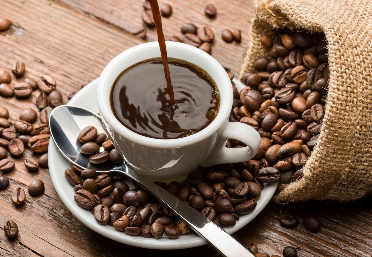 A cup of coffee being poured into a bag of coffee beans