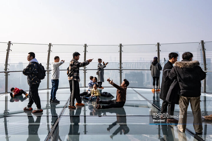 بازدیدکنندگان از یک سکوی رصدی به ارتفاع 250 متر در مجتمع رافلز سیتی مشرف به محل اتصال رودخانه های یانگ تسه و جیالینگ عکس می گیرند.